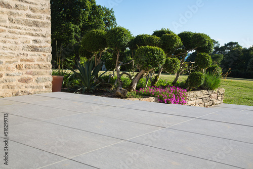 Modern garden design and landscaping:Hillside plot paved with natural sidewalk flagstones in contrast to a raised bed with natural stone walls, planted with succulents, flowers and beautiful boxtrees