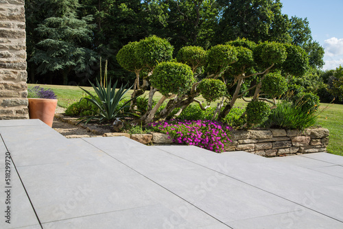 Modern garden design and landscaping:Hillside plot paved with natural sidewalk flagstones in contrast to a raised bed with virgon stone walls, planted with succulents, flowers and beautiful boxtrees