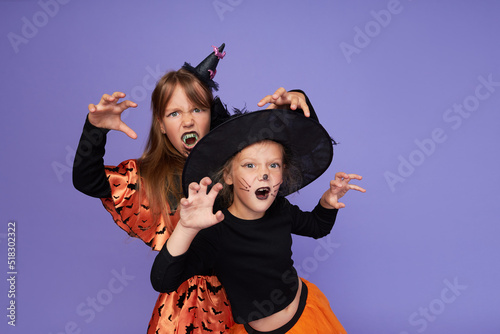 Funny children in carnival costumes of skeleton and witch in honor of Halloween on a purple background.