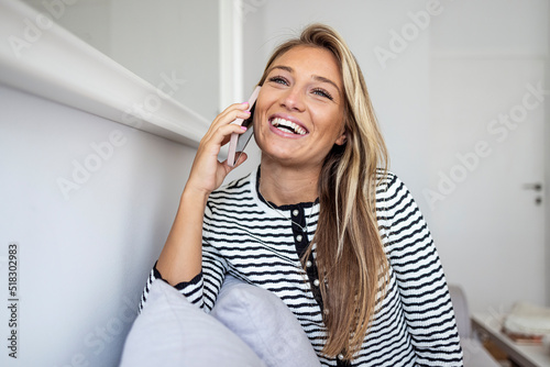 Woman talking on her mobile phone. Woman has a happy conversation at cellphone. Smiling woman using phone sitting on couch at home. Young woman talking on mobile phone and looking away.