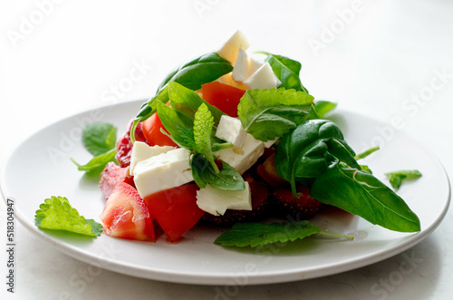 Vegetarian salad with tomatoes, cheese, strawberry, basil and mint on the white plate stock photo