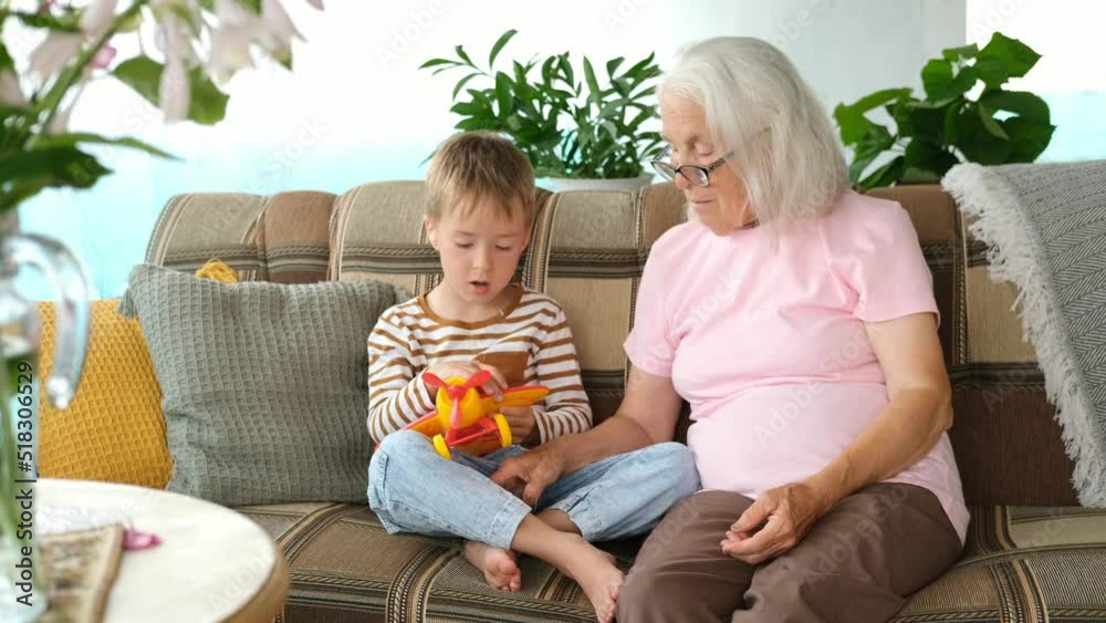 Little boy, grandson is sitting on couch with his grandmother and shows his toy airplane. Family weekend communication of generations. Little boy, grandson is sitting on couch with his grandmother and shows his toy airplane. Family weekend communication of generations.