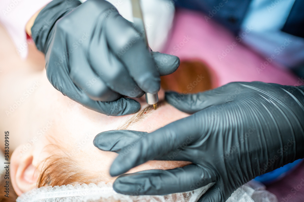 Procedure of eyebrow microblading. A master in black gloves is doing a blending needle of model's brow. Procedure of eyebrow microblading. A master in black gloves is doing a blending needle of model's brow.