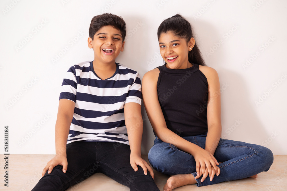 Cheerful boy and girl sitting together on floor against white wall Cheerful boy and girl sitting together on floor against white wall