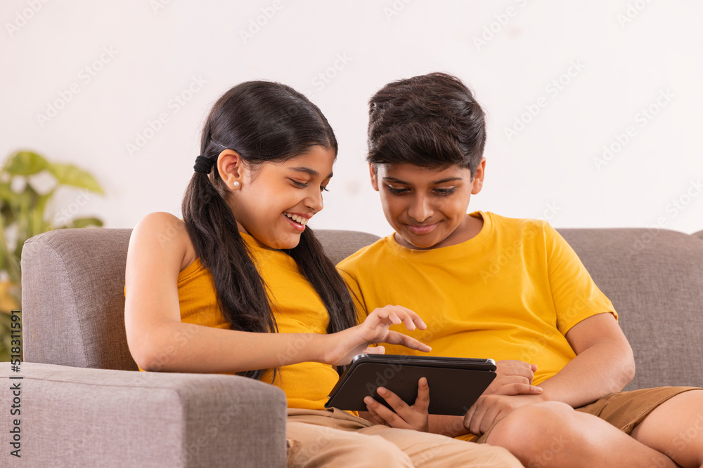 Fototapeta premium Boy and girl using digital tablet while sitting on sofa in living room