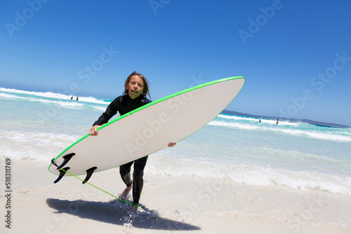 Child in wetsuit carrying surfboard out of the water photo