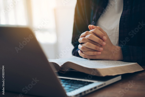 Women\'s hands are folded in prayer on a Holy Bible over a laptop in church concept for faith, religion, love, and forgiveness. Holy Bible study reading together in Sunday school.Online church