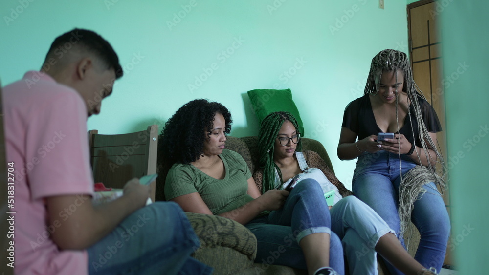 Fototapeta premium Candid group using phones sitting on couch. Four hispanic black friends looking at smartphones