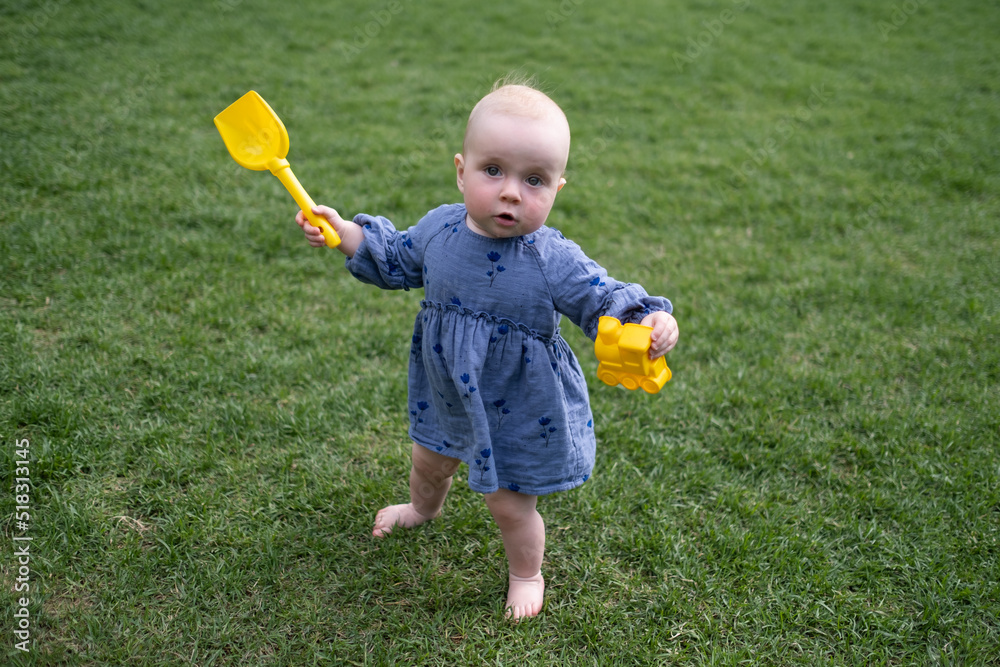 Φωτογραφία Child little girl study to go in the green lawn holding toys in hands