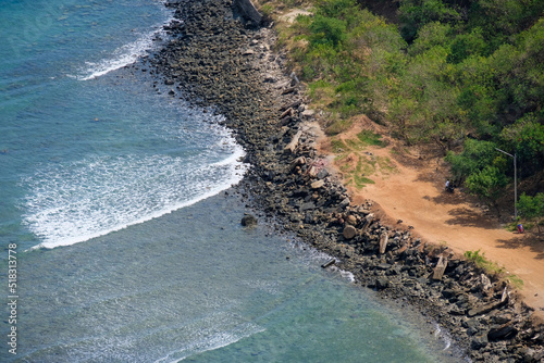 Waves rolling in along a rugged  rocky shoreline with red earth and trees on a remote tropical island  aerial view of stunning ocean landscape