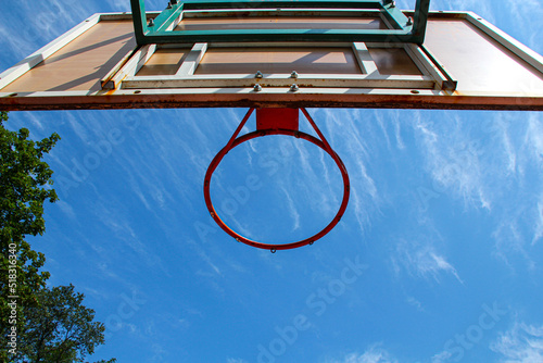 Basketball ring on the background a blue sky with white clouds and green tree. Basketball hoop on a shield on an outdoor sports ground. Basketball equipment. Copy space