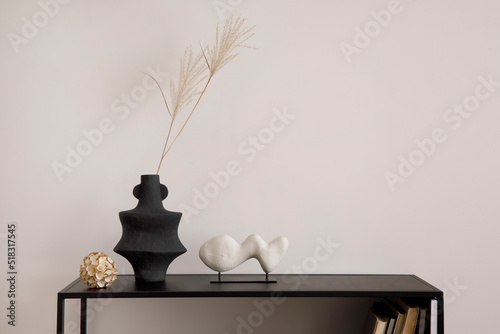 The stylish composition of minimalistic interior with copy space. White vase with dried flowers, sculpture and stylish accessories. Beige wall. Home decor. Template.