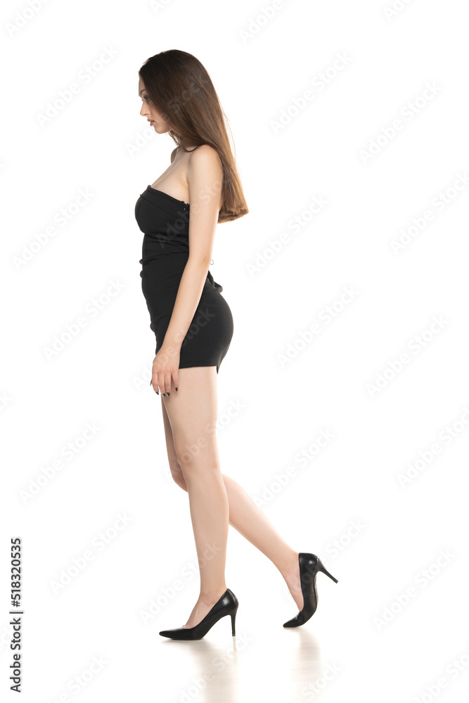 Side view of a young woman with short, black summer dress walking in the studio on white background Side view of a young woman with short, black summer dress walking in the studio on white background