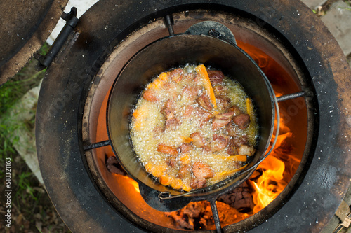 an elderly man cooks pilaf in a pot on a tandoor stove.