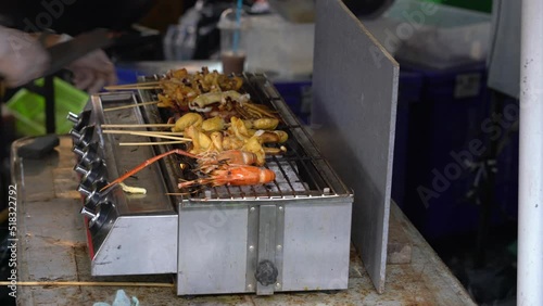 Person barbecuing seafood skewers at market in Bangkok. Local food stall photo