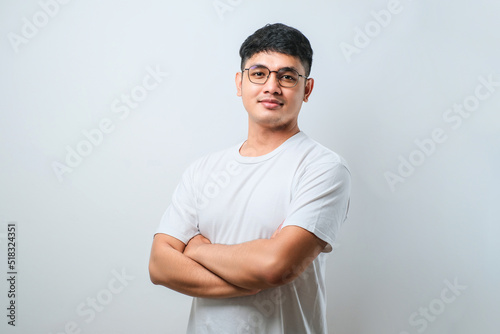 Portrait of young handsome Asian man wearing casual shirt and glasses standing with arms crossed and smiling at camera photo
