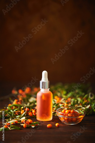 Glass bottle with sea buckthorn oil berries and sea buckthorn branches on wooden background photo