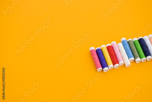 Different colorful sewing threads on yellow background, flat lay © ALEXSTUDIO