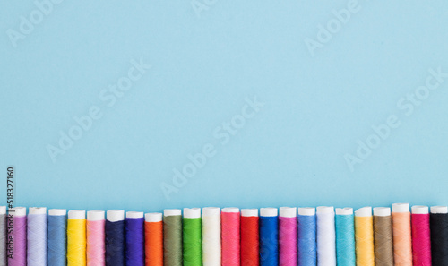 Panoramic detailed view of multi colored spools of thread on a blue background.