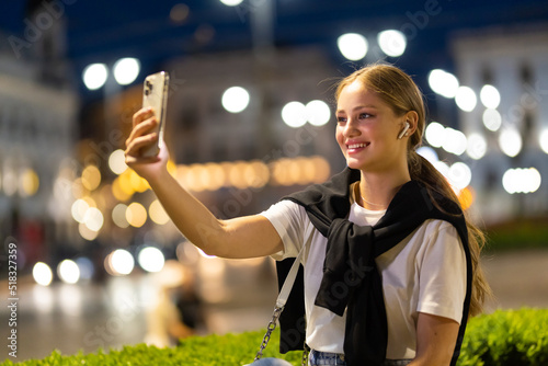 Smile girl using mobile smartphone on background bokeh light in night city taking selfie photo