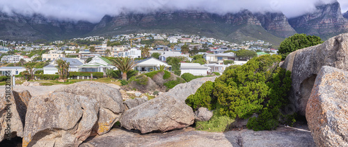 Rocks and boulders against a majestic mountain and cityscape background with lush green plants and coulds. Remote and quiet landscape on a cliff with stones to enoy a urban view with private homes photo