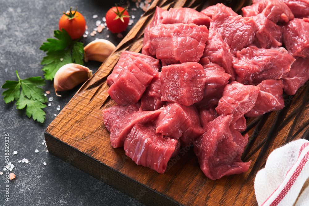 Raw chopped beef meat. Raw organic meat beef or lamb, spices, herbs on old wooden board on dark grey concrete background. Goulash.  Raw uncooked meat. Meat with blood. Top view with copy space.