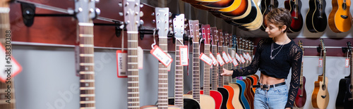 Young woman choosing acoustic guitar in musical store, banner.