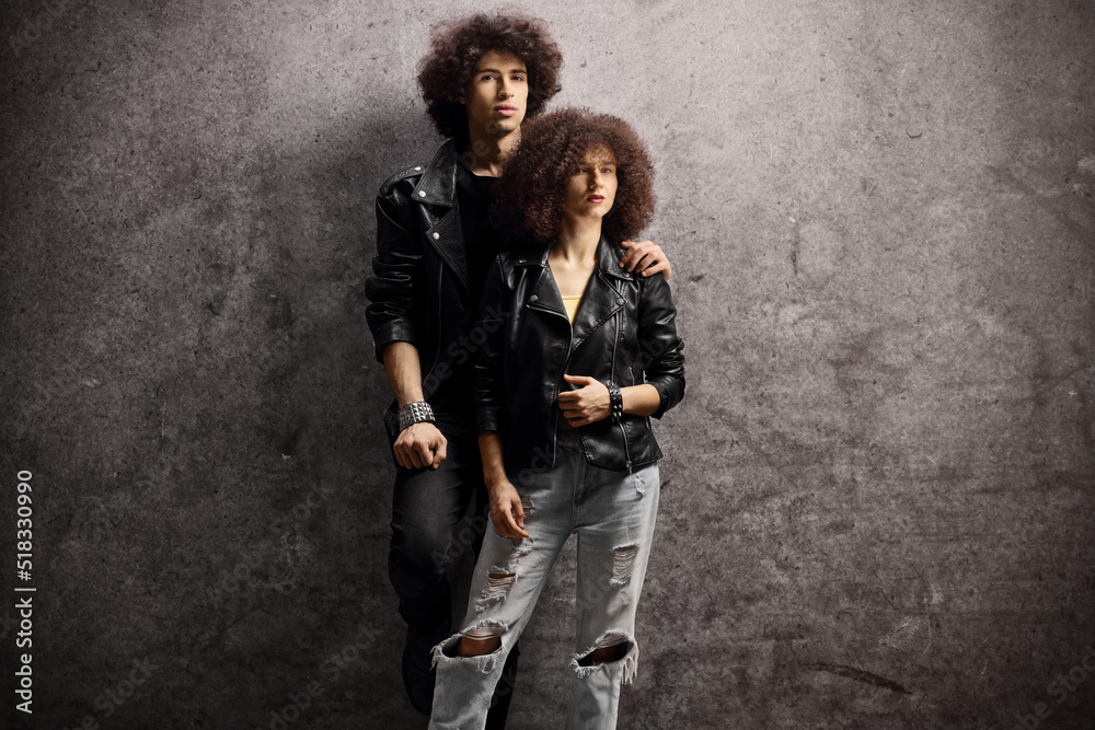 Young man and woman with leather jackets and curly hair leaning on a dark background