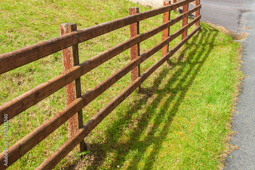 Perspective from the border fence, across the green lawn on a summer day. The border of the land plot is made of wooden slats. The passage is closed.