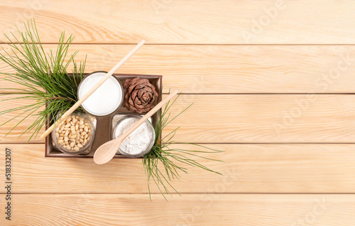 Cedar milk, flour, nuts, cone, branches in wooden box on wooden table. Banner. Top view. Copy space.