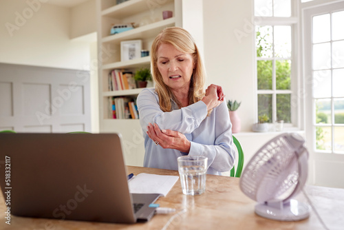 Menopausal Mature Woman Suffering Elbow Joint Pain Working On Laptop At Home