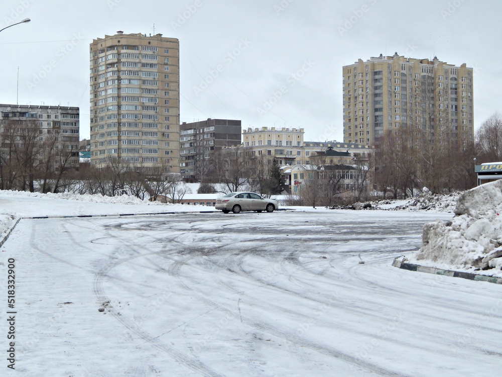 Several tall buildings and a car in a snow-filled parking lot.