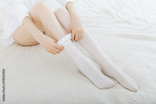 Girl putting on white stockings at home. Anti-embolic stockings. Compression Hosiery. Medical stockings, tights, socks, calves and sleeves for varicose veins and venouse therapy