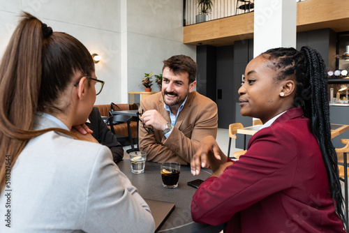Fotografie Group of young perspective freelancer business people sitting at cafeteria having meeting about opening private small company as equal partners and to hire young people with ideas for full time work