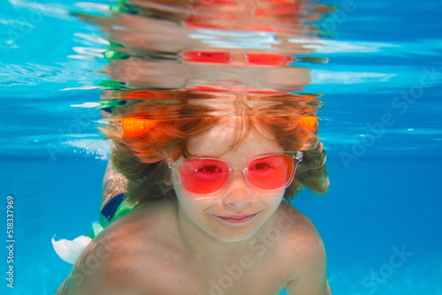 Summer kids face. Young boy swim and dive underwater. Under water portrait in swim pool. Child boy diving into a swimming pool. © Volodymyr