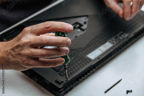 close-up of the repairman's hands unscrewing the screws from the laptop case with a screwdriver for its repair and maintenance. repair and maintenance of laptops. selective focus.