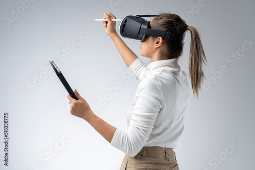 White shirt woman wearing VR glasses holding tablet and pen gesturing in the virtual world. © PIPAT