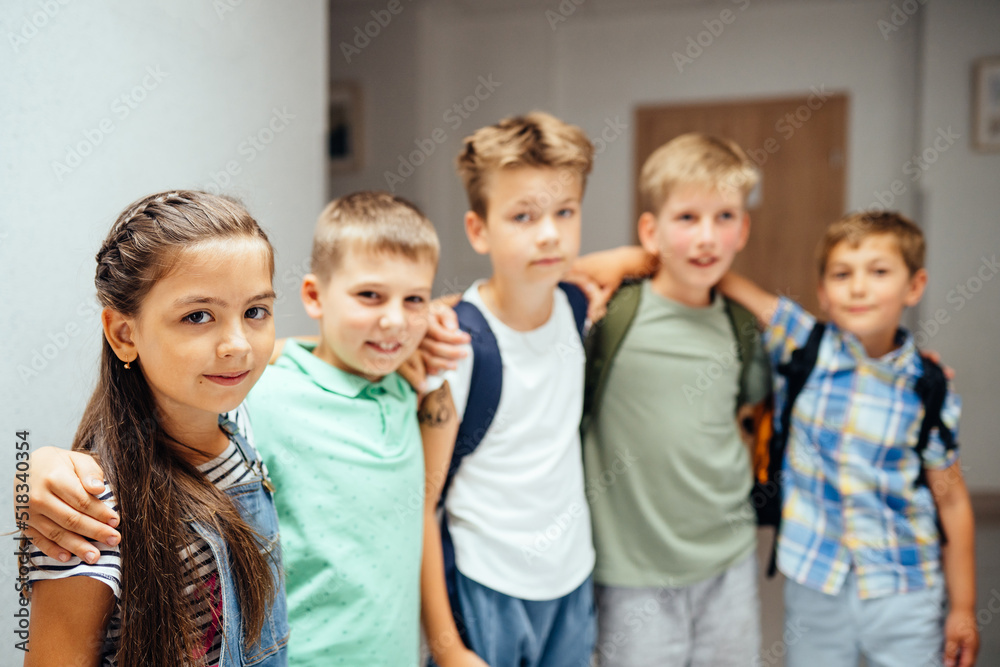 Group of five schoolmates children standing together and hugging during break at school. Focus on hispanic girl. Children are happy to go back to school after the holidays Group of five schoolmates children standing together and hugging during break at school. Focus on hispanic girl. Children are happy to go back to school after the holidays