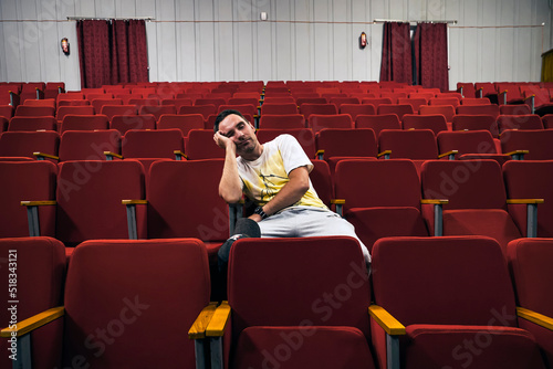 A lonely young man in an empty theater fell asleep at the performance. An uninteresting boring opera.. man with glasses sleeping alone in cinema hall while everyone is gone