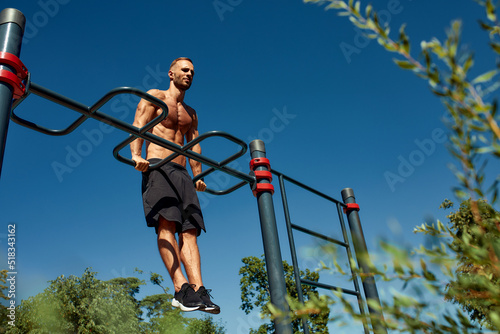 Handsome man on sport ground. The sportsman the guy, carries out difficult exercise, sports gymnastics. Muscular man doing workout. The concept of a modern young man