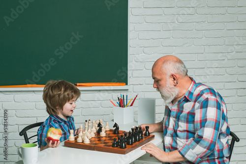 Grandfather and grandson boy playing chess, men generation. Different ages, grandfather and child grandson study chess together in home classroom.