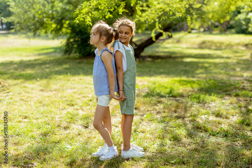 Two little girls standing back to back in the park