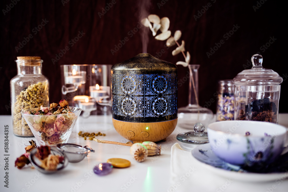 Fototapeta premium Essence diffuser in wood and metal with several jars of dried flower infusions (lavender, roses and chamomile), a cup of tea and a candle holder..