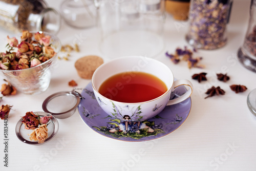 Cup of tea with jars of lavender infusion, star anise and dried roses.