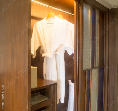 Two elegant white bathing gowns hanging in wardrobe in hotel nicely prepared to serve for guests
