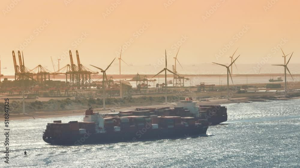 Container ship entering the port of Rotterdam from the North Sea and is sailing towards the container terminal. Aerial view drone footage from above.