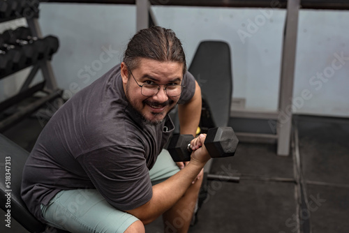 A man in his late 30s makes a comeback at the gym. Doing seated dumbbell concentration curls with a relatively light weight. A dad getting back in shape. photo