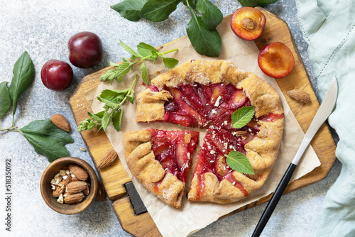 Plum Galette. Healthy homemade wholegrain fruit pie (galette) with plums and almonds, vegan vegetarian dessert on a stone table. View from above.