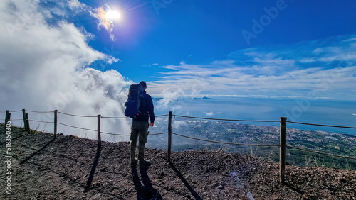 Man with backpack enjoying scenic view from volcano Mount Vesuvius on bay of Naples, Province of Naples, Campania, Italy, Europe, EU. Looking at city of Naples and Mediterranean coastline on sunny day photo