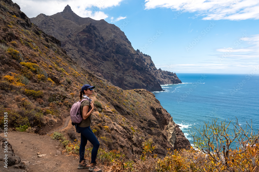 Backpack woman on hiking trail from Afur to Taganana with scenic view of Atlantic Ocean coastline and Anaga mountain range, Tenerife, Canary Islands, Spain, Europe. Looking at Cabezo el Tablero crag